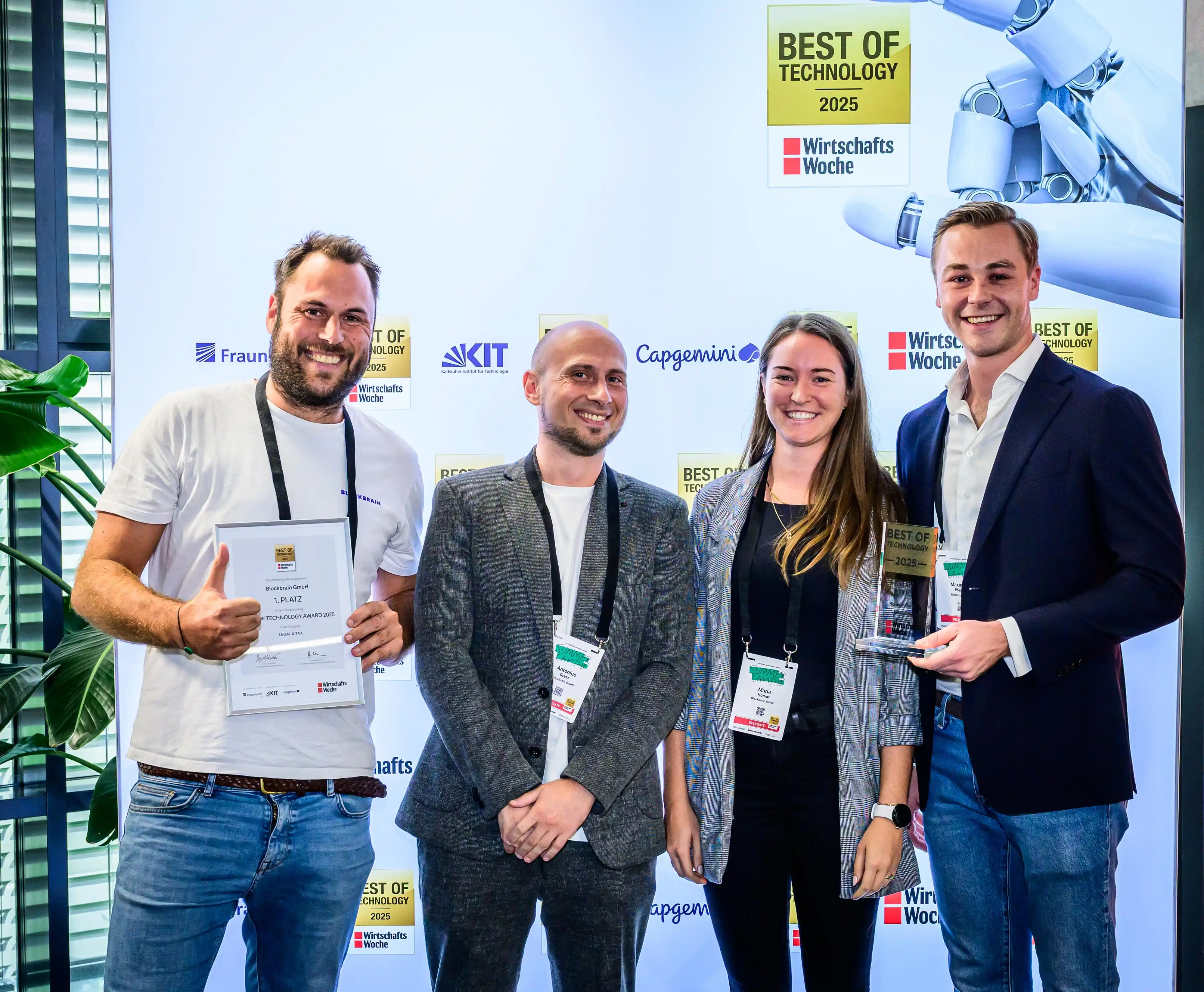 Four people at a technology award event holding certificates and trophies, standing in front of a branded backdrop