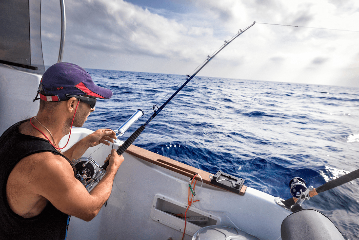 Man in a cap deep-sea fishing from a boat on the open ocean.