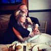 A couple sitting together, smiling at a table, embracing warmly.
