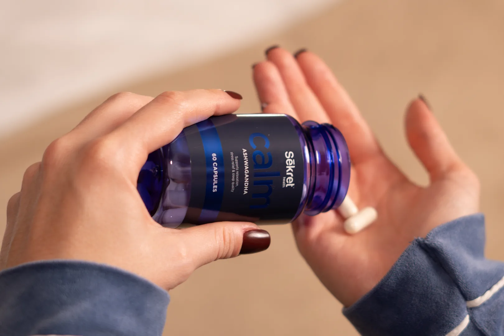 A capsule tipped from a bottle of Sēkret Calm into an open hand at home