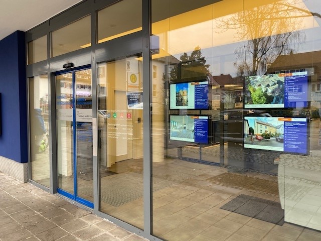 Storefront with automatic glass doors and multiple digital real estate displays.