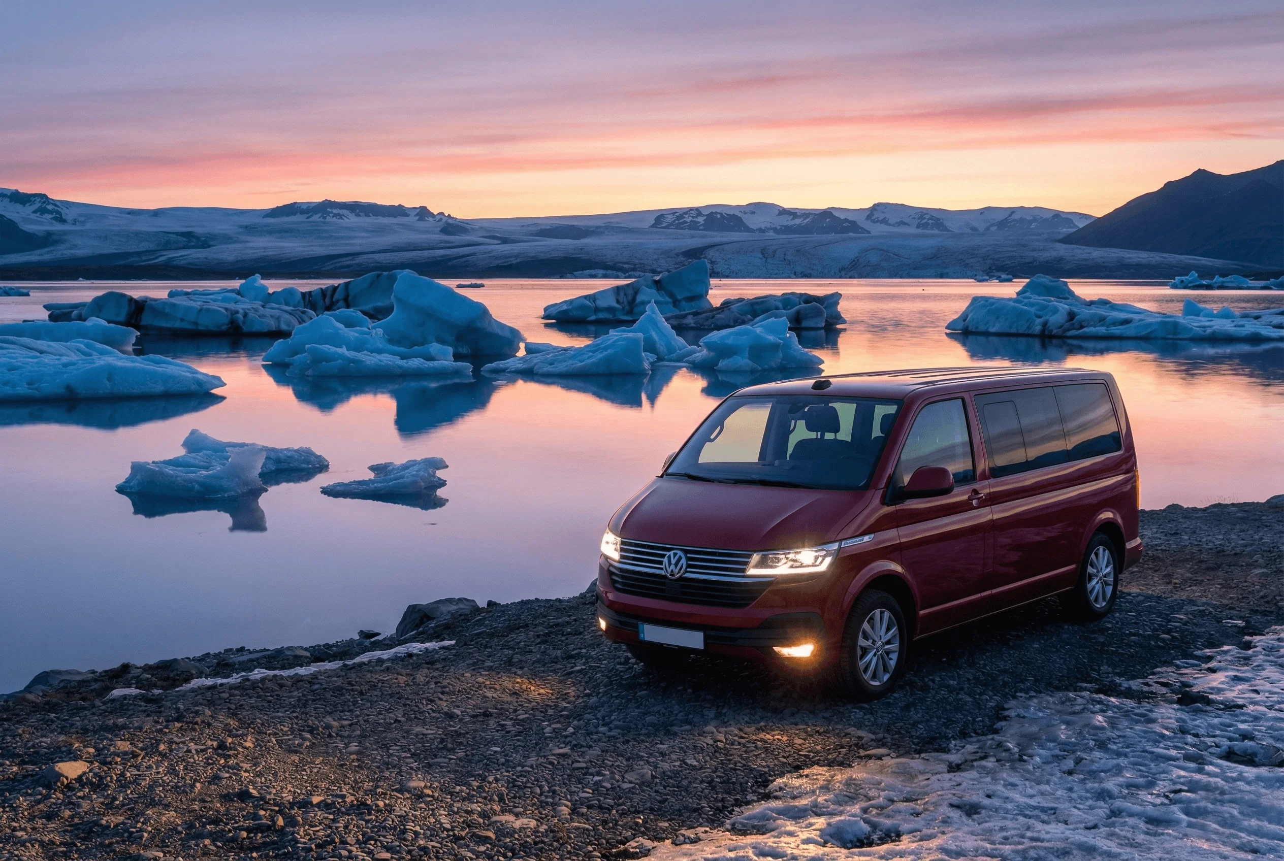 A red camper van parked on the shore of a glacier lagoon filled with blue icebergs at twilight.