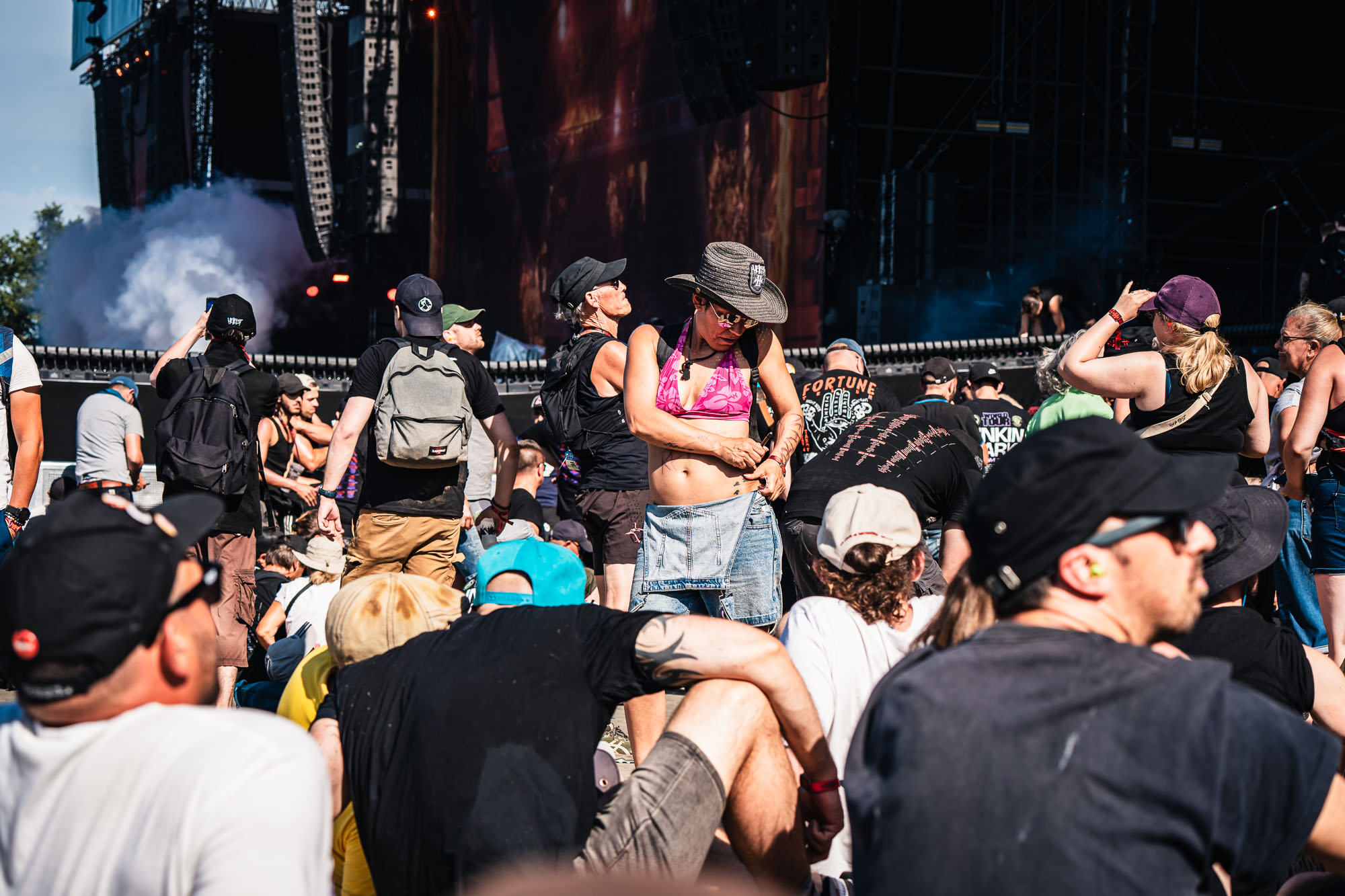 Festivalière en chapeau et haut fluo assise dans la foule, ambiance festive de jour