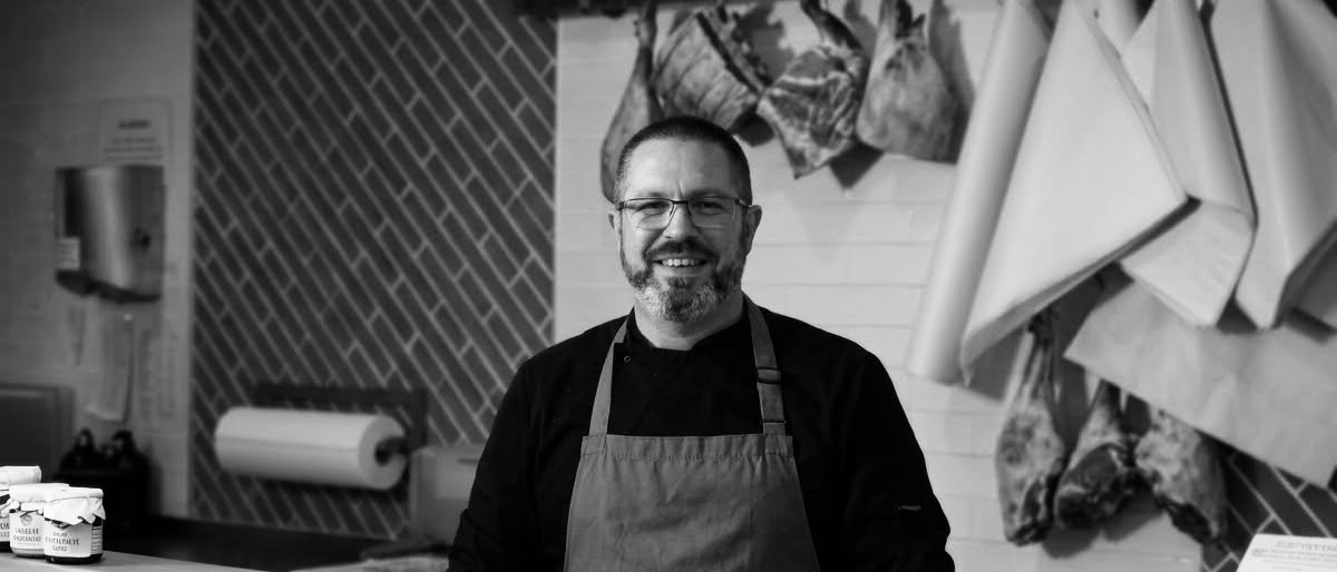 A smiling Hayden & Baker butcher behind the counter in the Ashtead shop