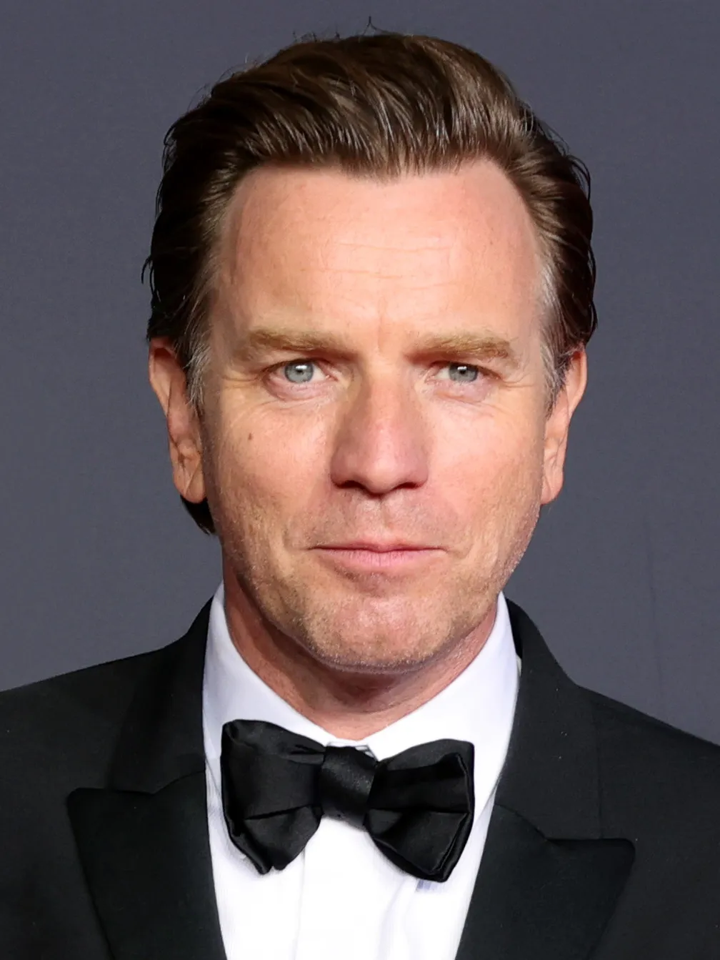 Minimalist profile shot of a man with long braids and a white shirt, set against a soft, light background.