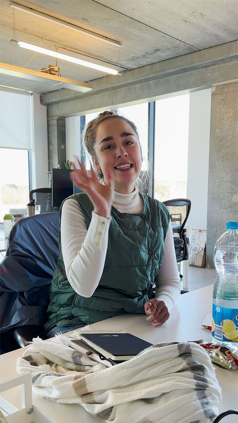 A person in an office smiles while talking on the phone, surrounded by paperwork and office supplies.