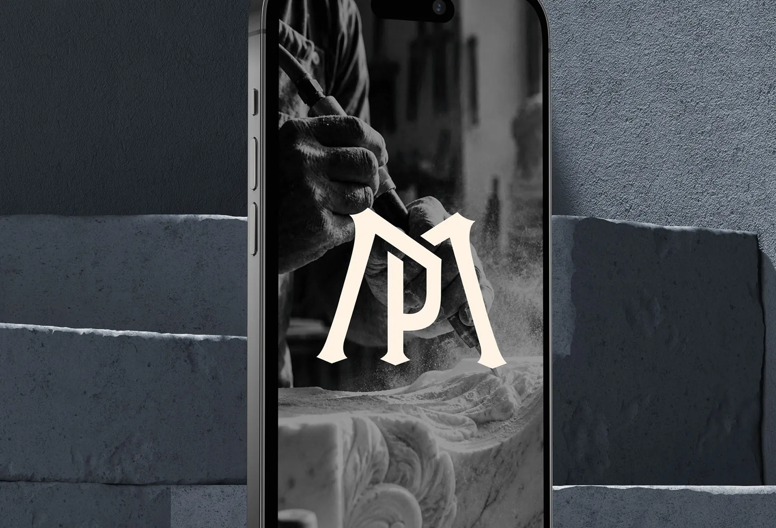 Monogramme M·P de Mémoire de Pierre affiché sur un téléphone, devant des blocs de pierre