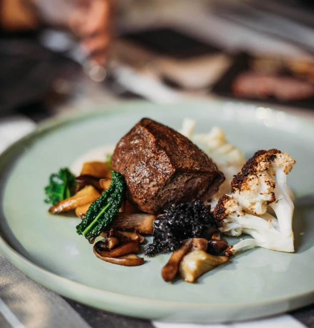 A gourmet dish featuring a thick cut of steak served with roasted cauliflower,