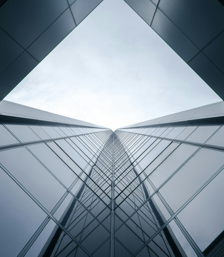 Upward view of a modern glass skyscraper with a geometric perspective, reflecting the sky and surroundings.