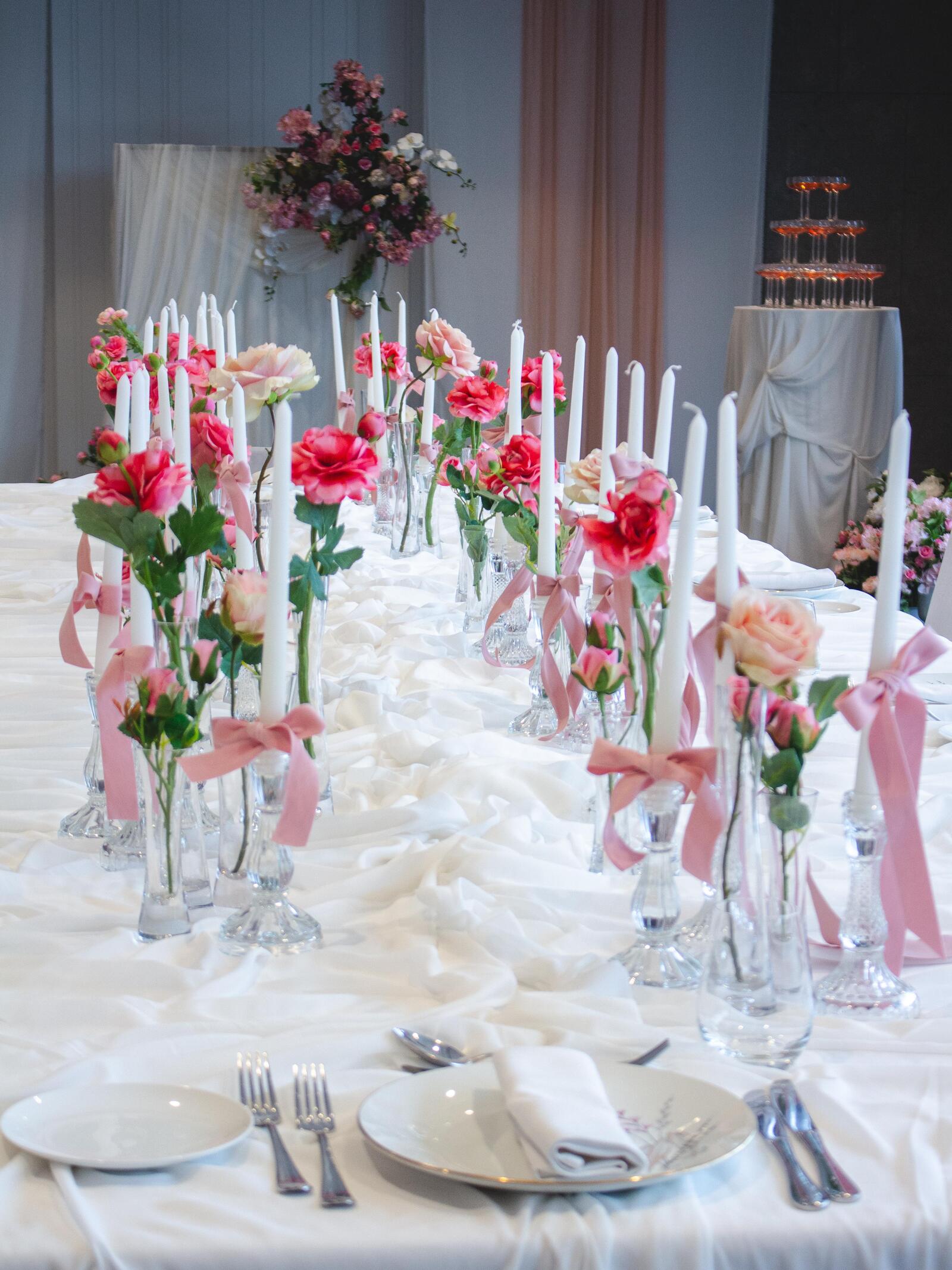 Long celebration table with pink flowers, white candles and a champagne tower