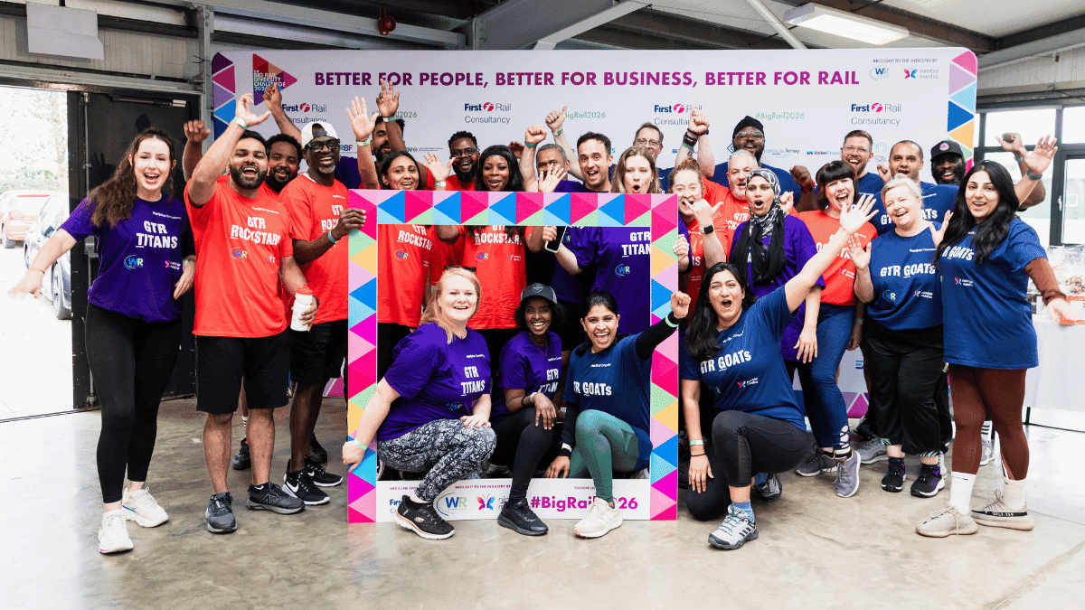 Team posing for a photo in front of the sponsor wall at the Big Rail Diversity Challenge.