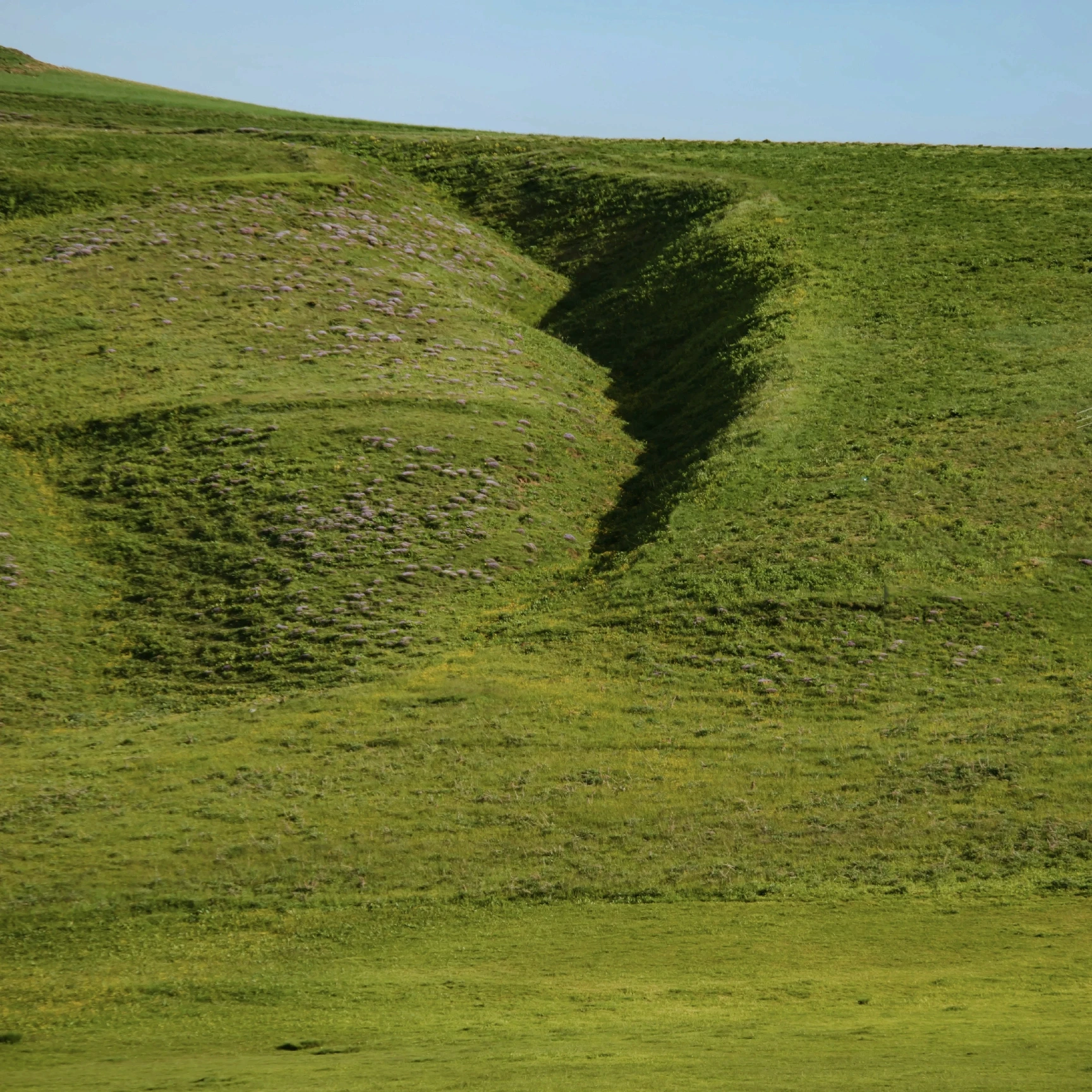 A green steep hill with skies in the background