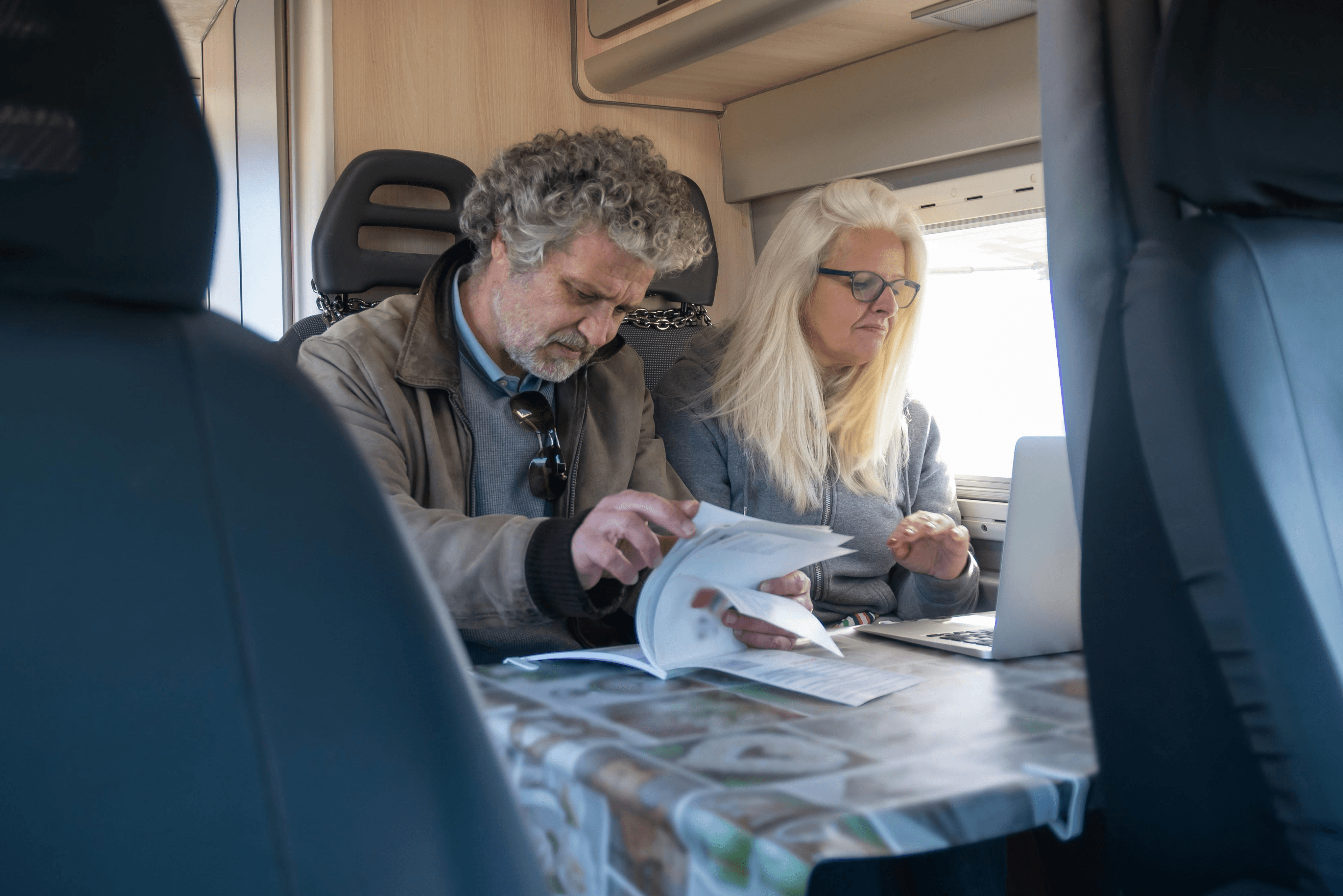 Independent RV park operators reviewing business documents and using a laptop inside a motorhome.