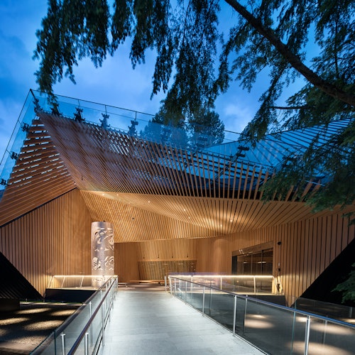 現代建築配有木條和玻璃欄杆，環境被樹木圍繞，黃昏時分燈光點亮。