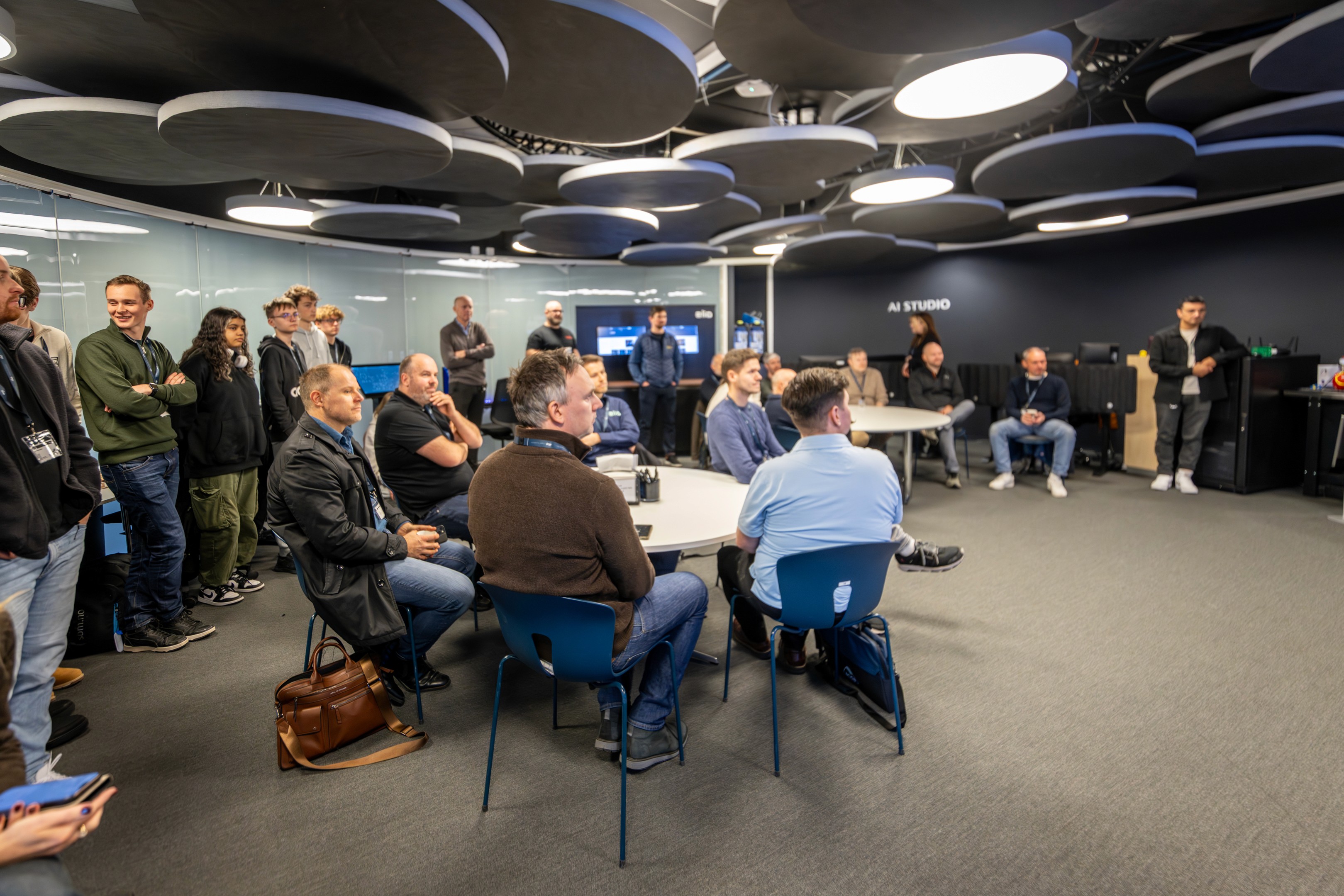A person wearing a virtual reality headset stands in front of multiple screens, engaged in a digital experience.