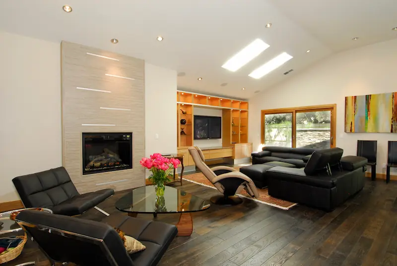 Modern living room with stone clad fireplace, black leather couches and dark hardwood flooring. Irvine Transitional Modern Project. Photo by Chris Darnall.