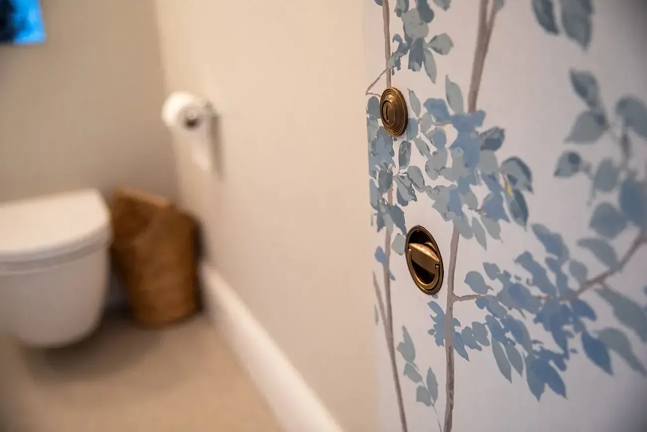 Close up of a floral print door with gold knobs, toilet, and a decorative bin in bathroom.