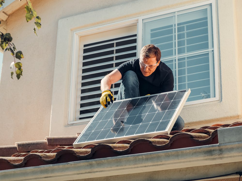 Free Solar technician installing a photovoltaic panel on a rooftop, promoting renewable energy. Stock Photo