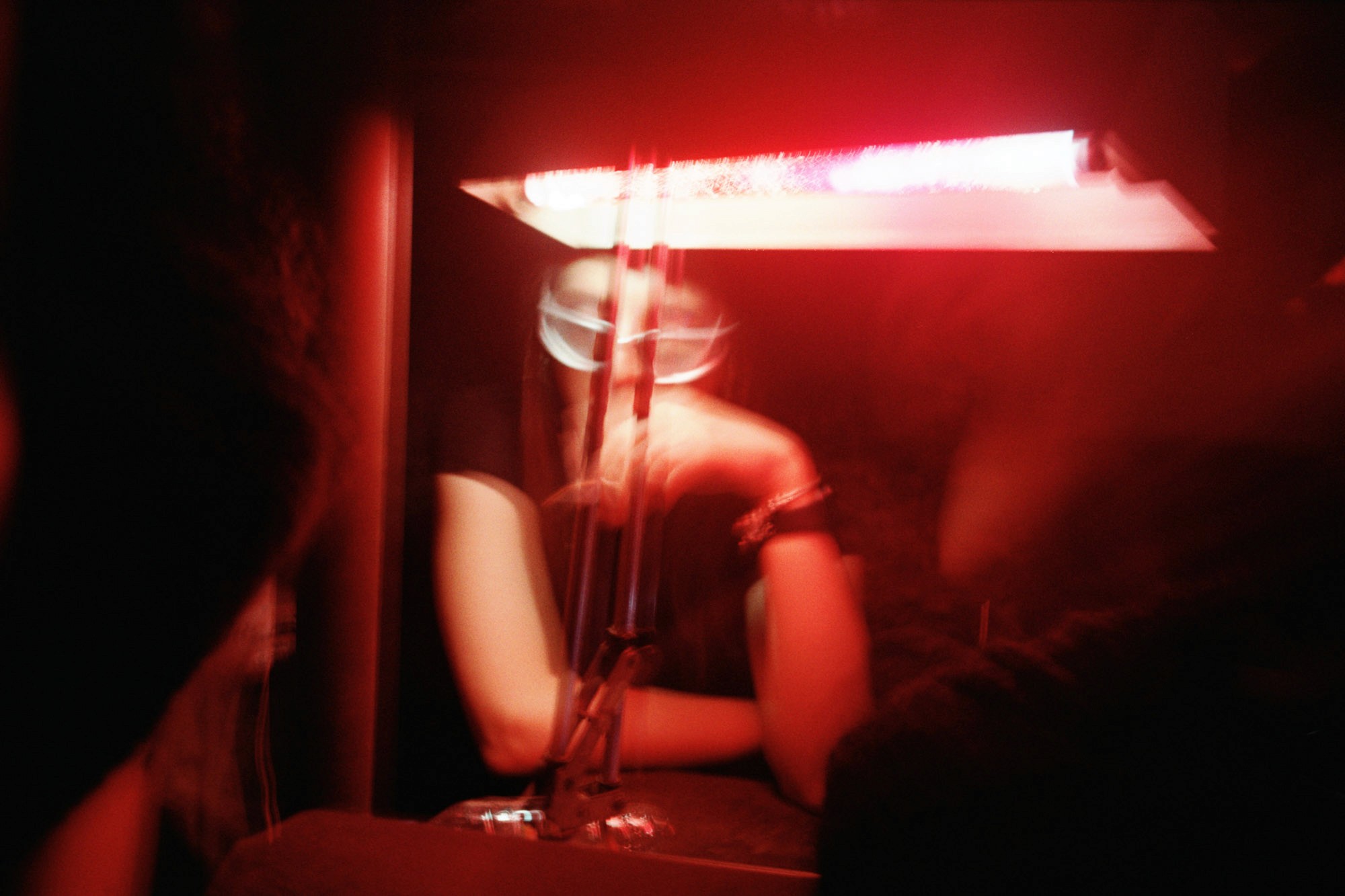 A person sits in a dimly lit room, with a neon red light casting a mysterious glow, creating an abstract and blurred effect around the surroundings.
