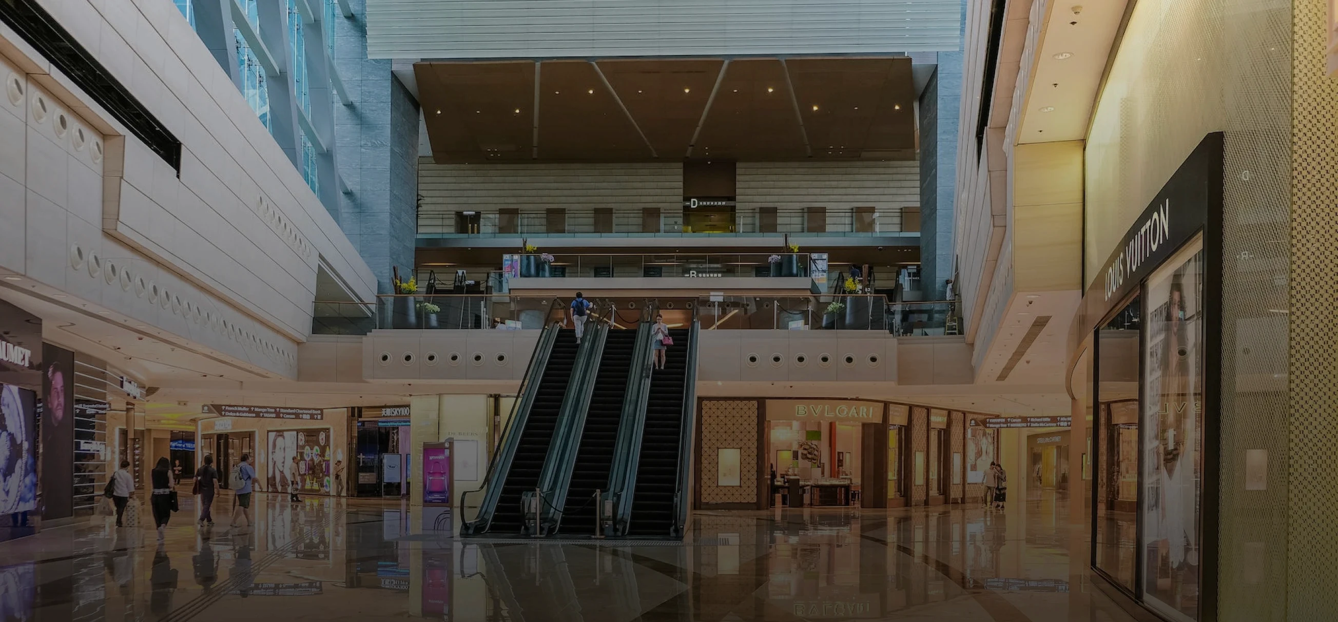 imagem de shopping center com algumas lojas nos lados e no centro da imagem uma escada rolante.