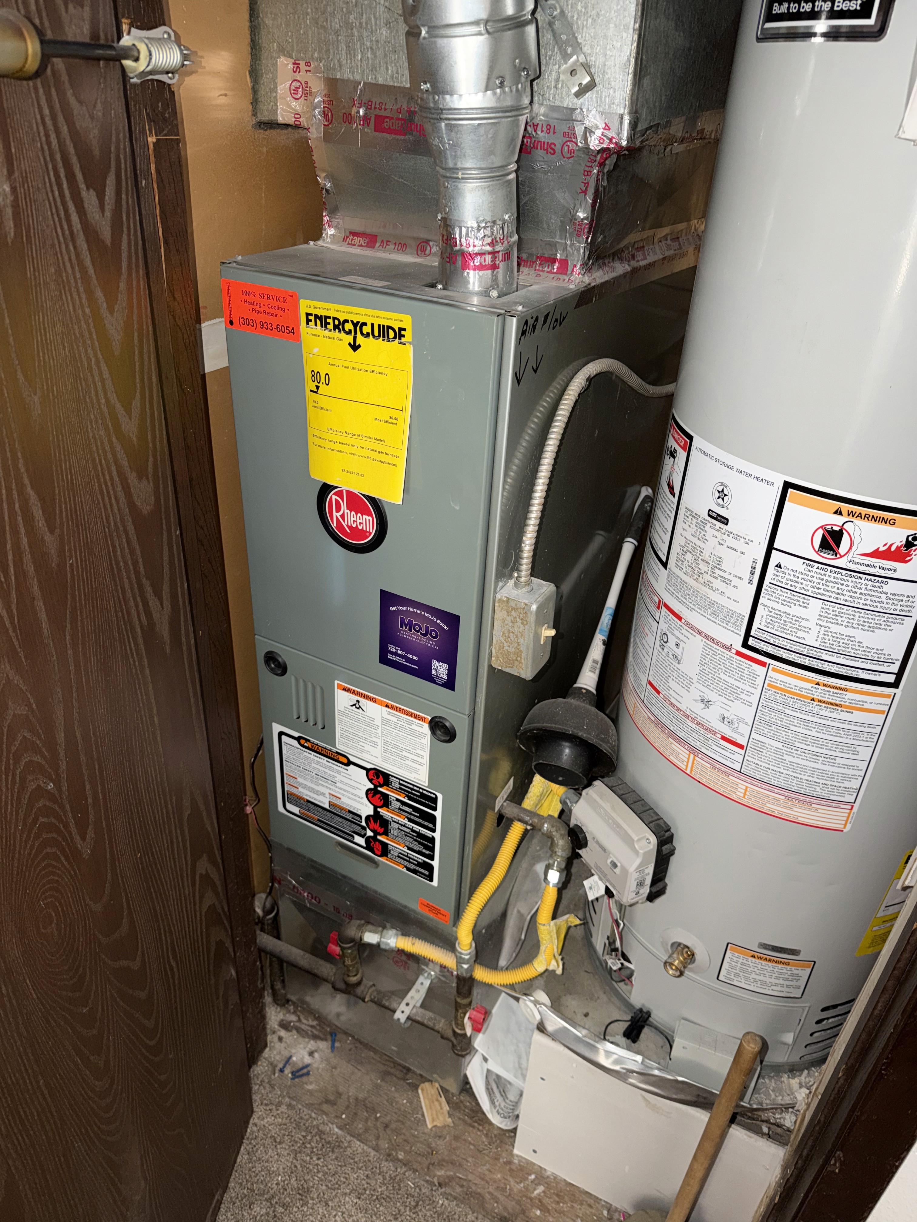 The image displays a residential heating system, specifically a furnace and a water heater, both manufactured by Rheem.