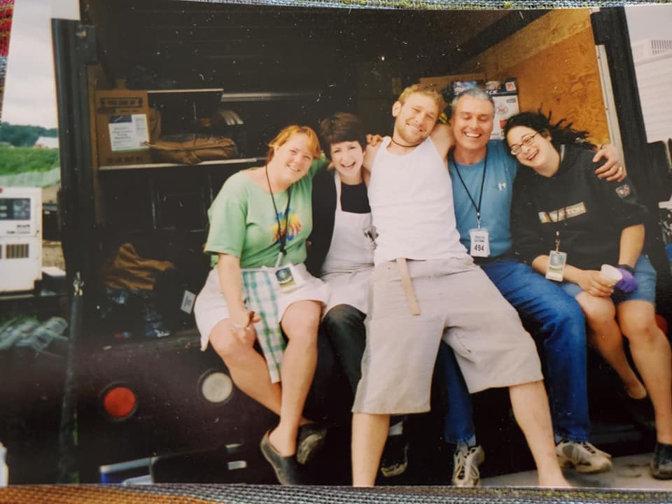 A group of five people posing playfully in front of a vehicle, all smiling and having fun together.