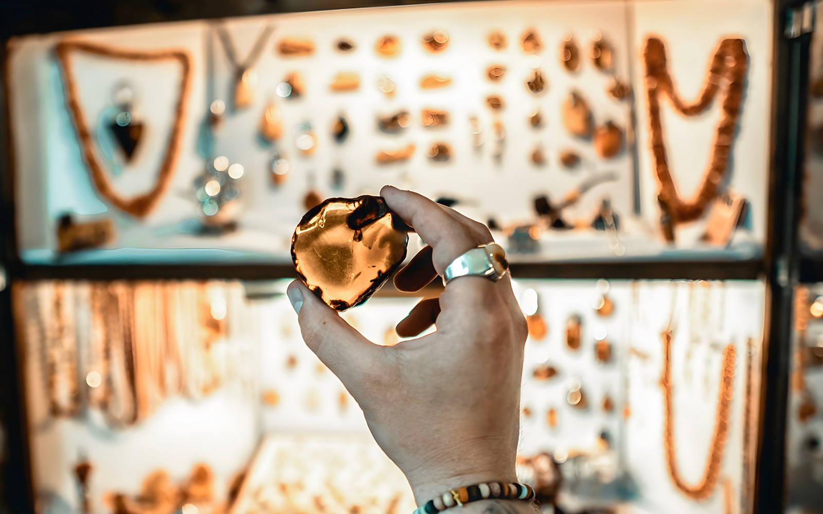 Hand holding amber piece in Gdańsk workshop with jewelry display in background.
