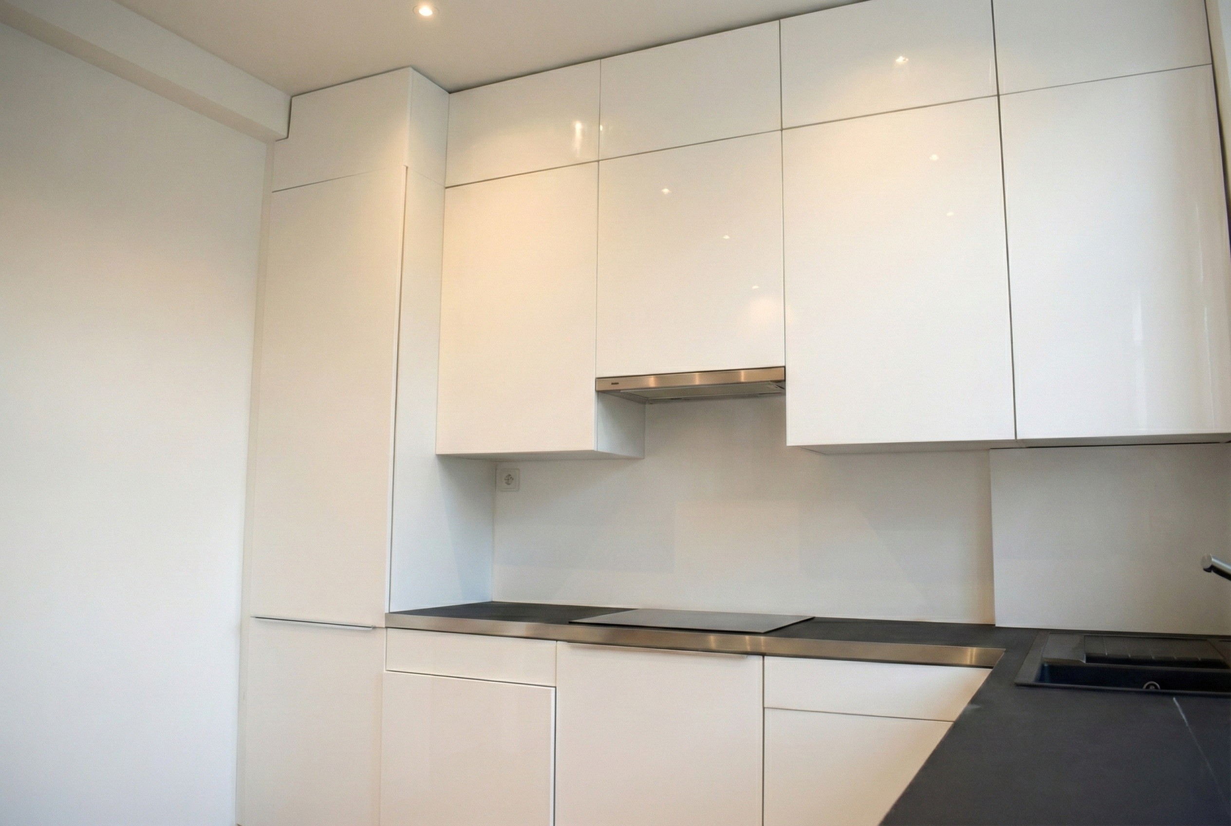 Cuisine contemporaine épurée avec façades laquées blanches, plan de travail sombre et éclairage intégré.