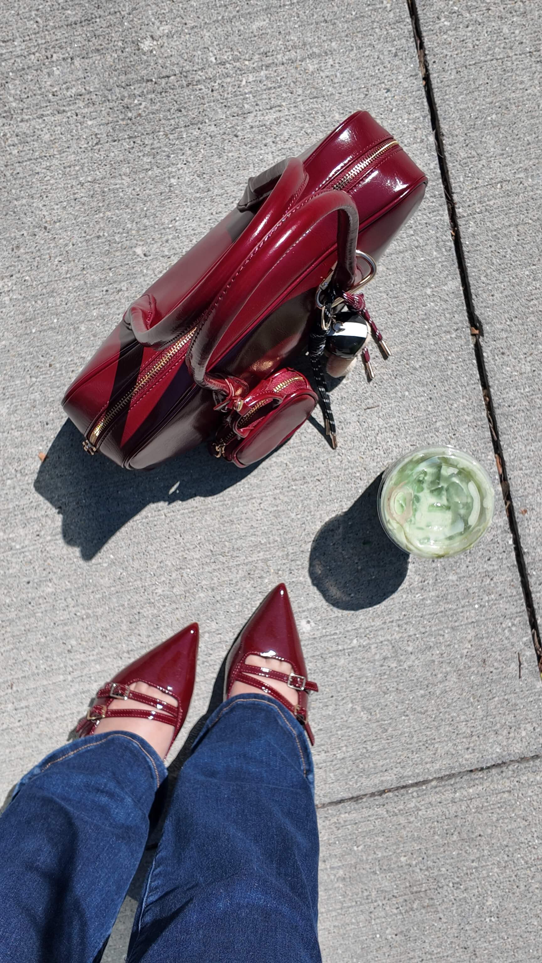 a photo of a red purse and matcha latte on the groud next to a woman wearing blue bootcut jeans and pointy red flats