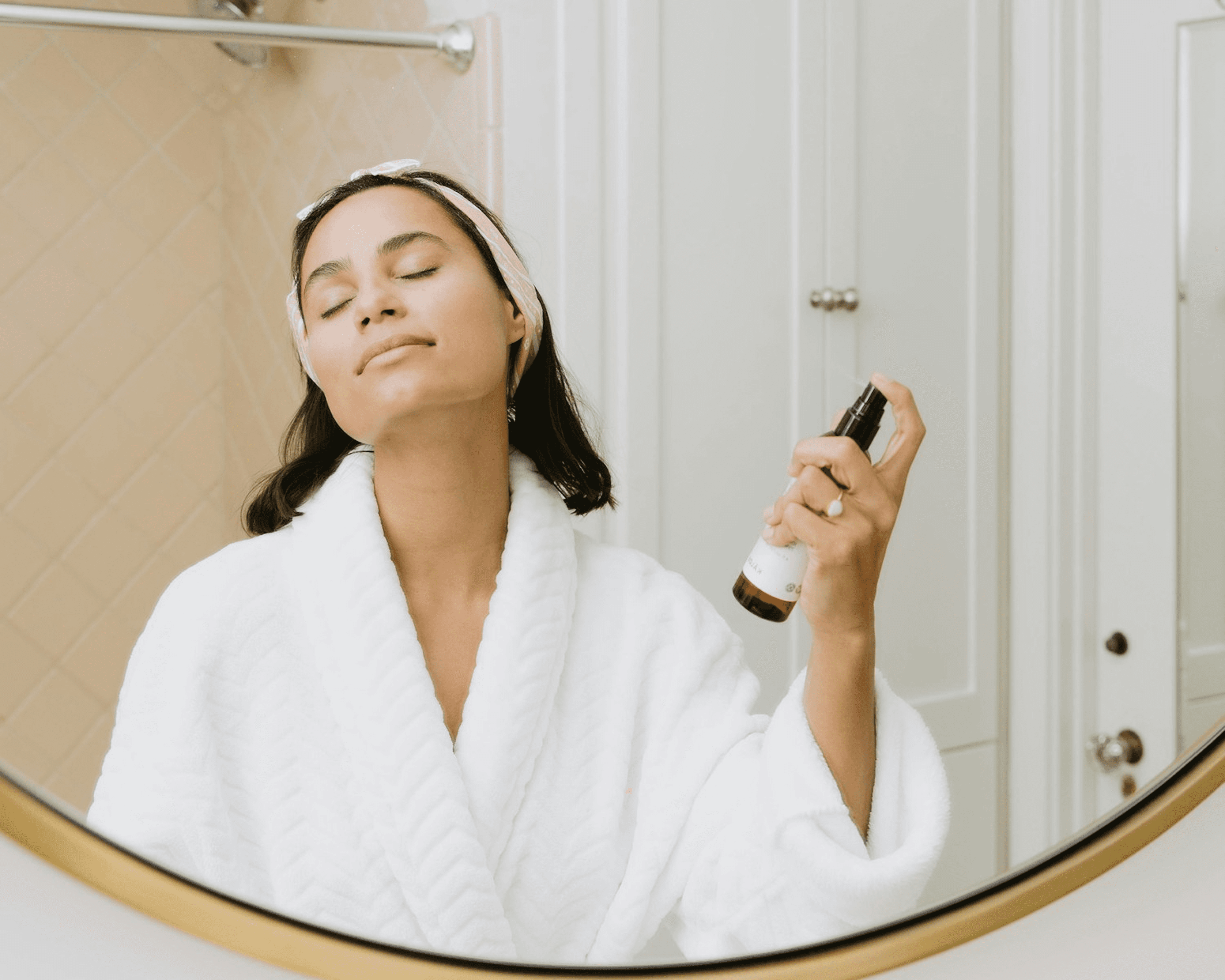 Person in bathrobe spraying facial mist in bathroom