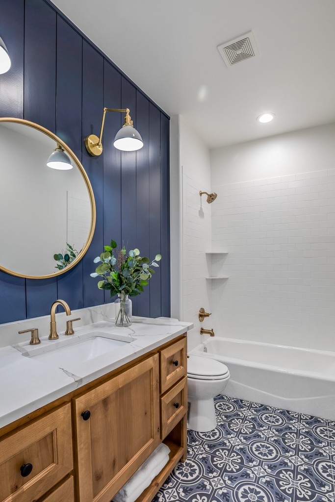 Custom bathroom vanity with wood cabinetry, brass fixtures, round mirror, and modern lighting in a renovated home