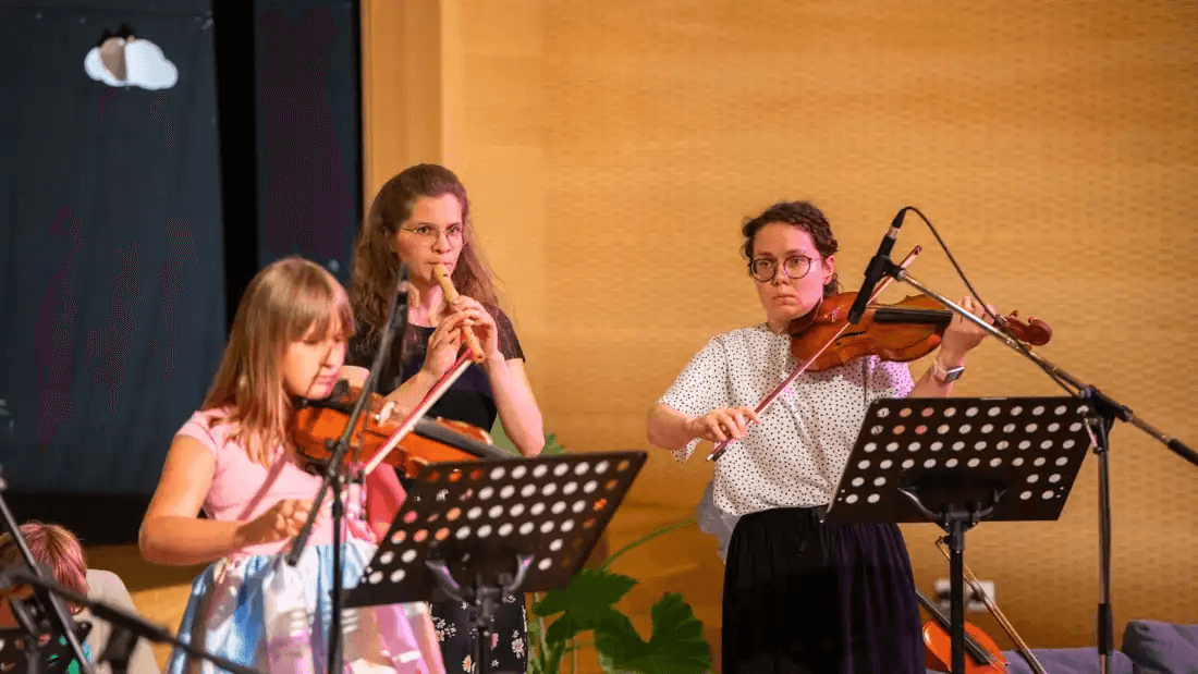 Učenka z violino nastopa na odru skupaj z mentoricama