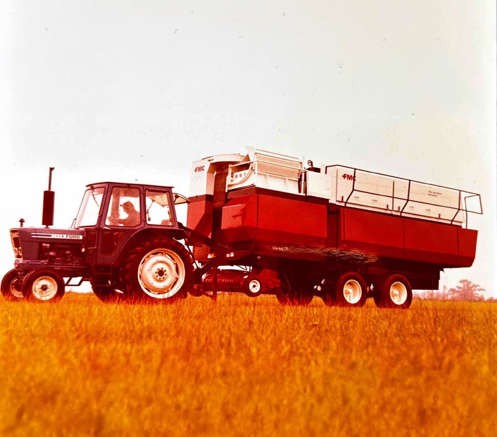 A vintage colour photograph of a Ford tractor pulling a red FMC pea harvester through a crop field, representing the harvesting technology of the era.