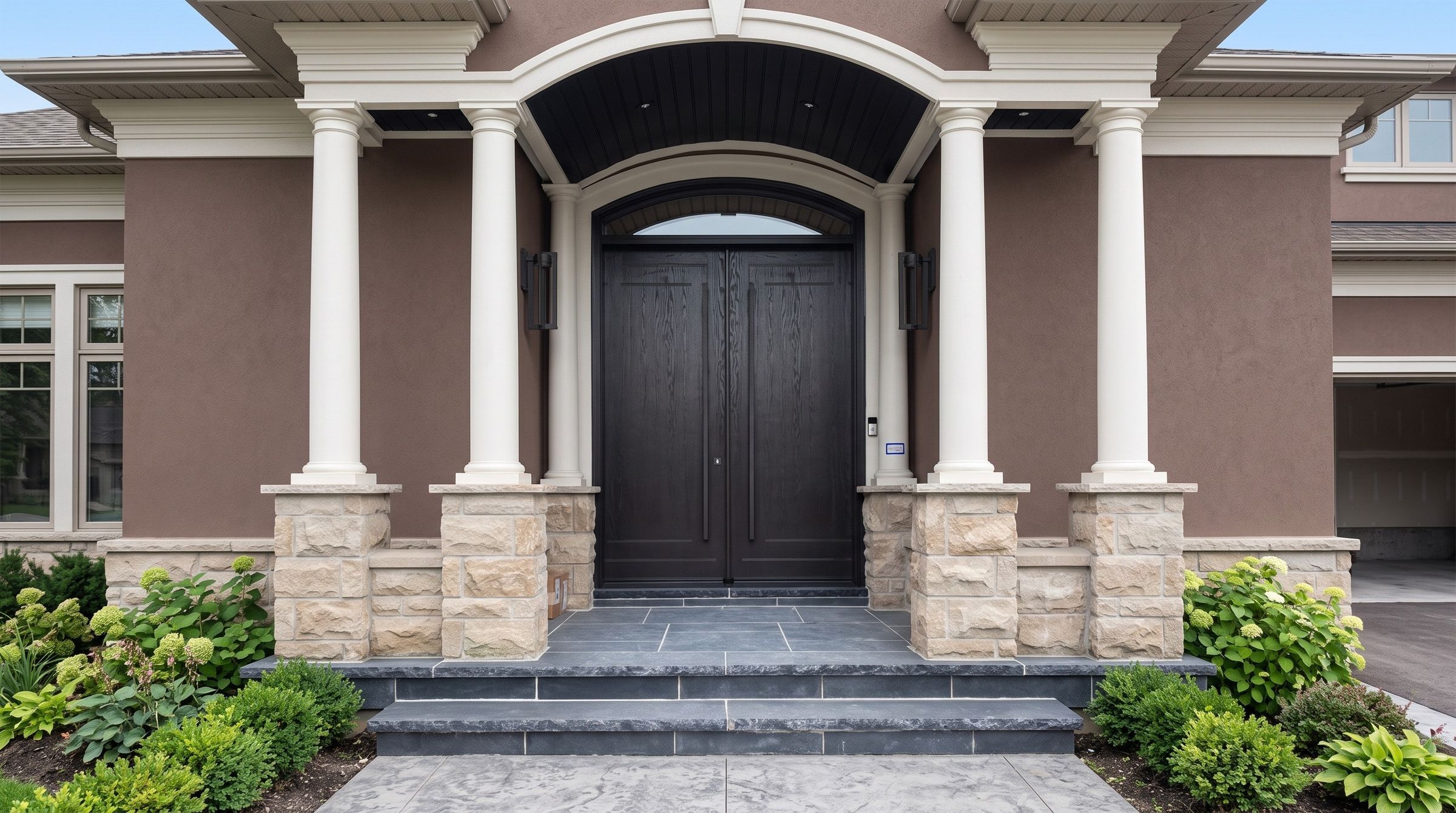 Custom dark wood-look fiberglass front door with arched top framed by white columns on an Ontario home
