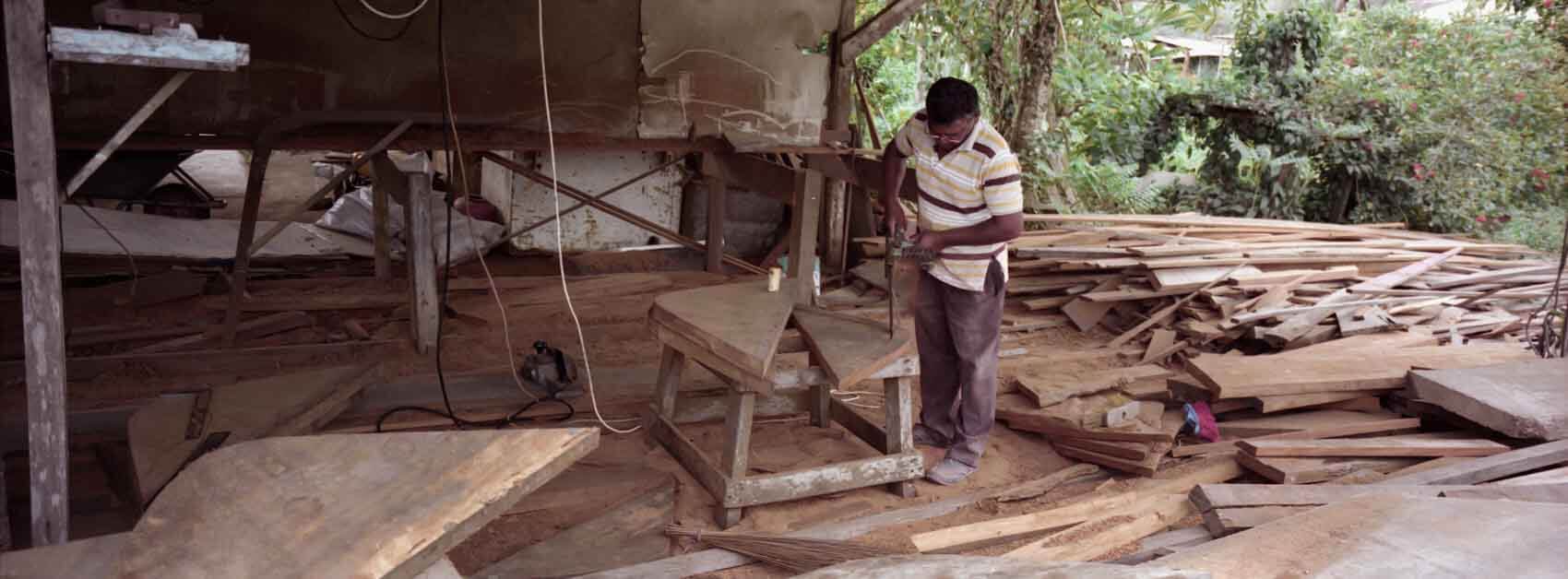 Traditional wooden boat builder in Suriname working inside a workshop, framed by wood, soft directional light shaping the scene, photographed on a Hasselblad Xpan and Kodak Portra. 