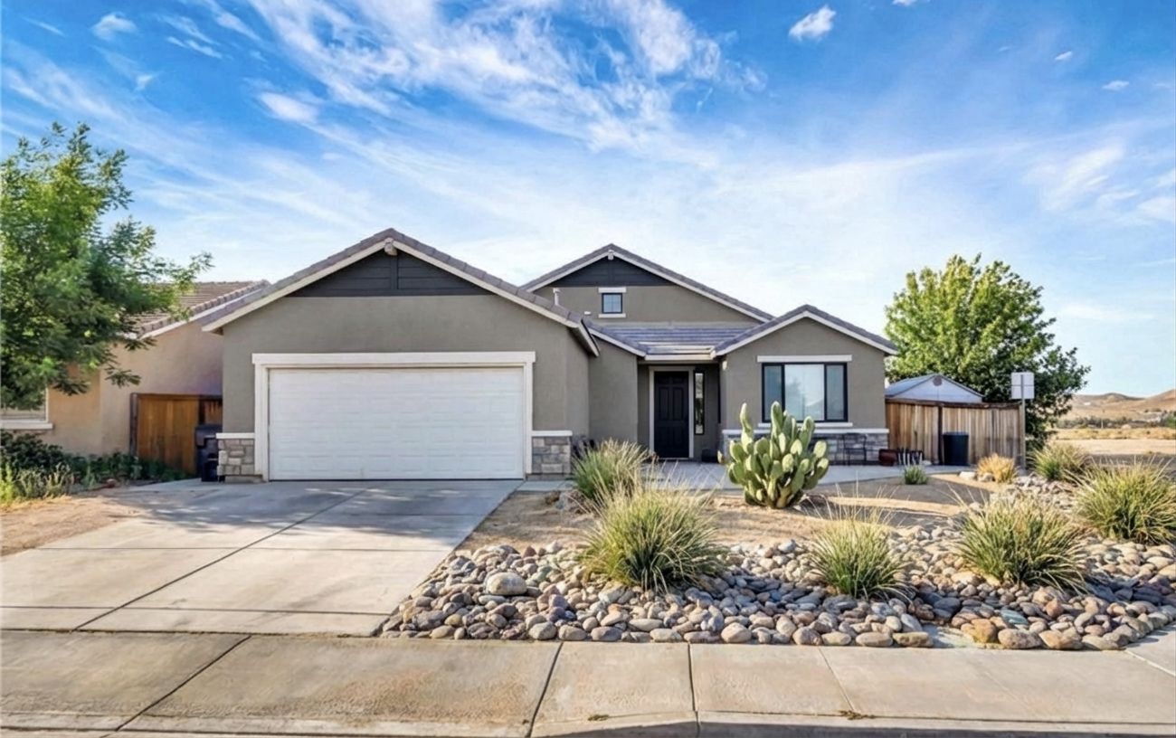 Modern desert minimal — warm gray stucco, charcoal gable planks, black door, river rock landscaping