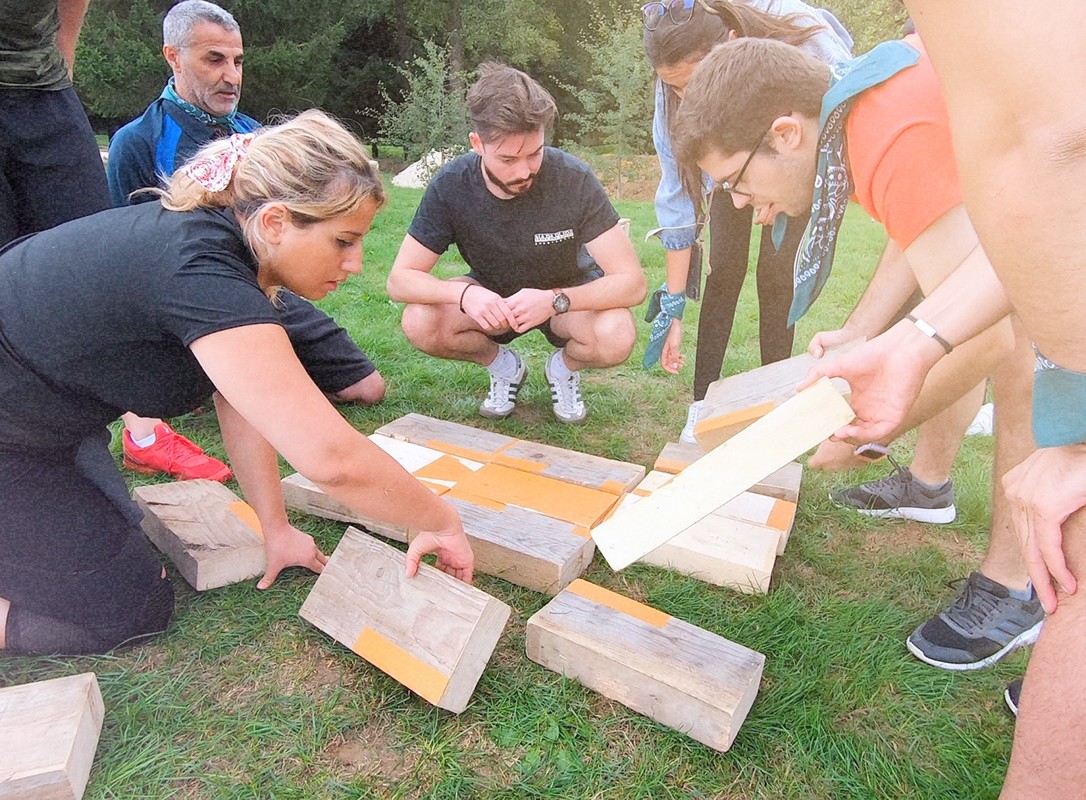 Plusieurs personnes s'agenouillant pour organiser des blocs de bois. L'image montre un homme et une femme en train de manipuler des pièces de bois pendant qu'un autre homme regarde attentivement.