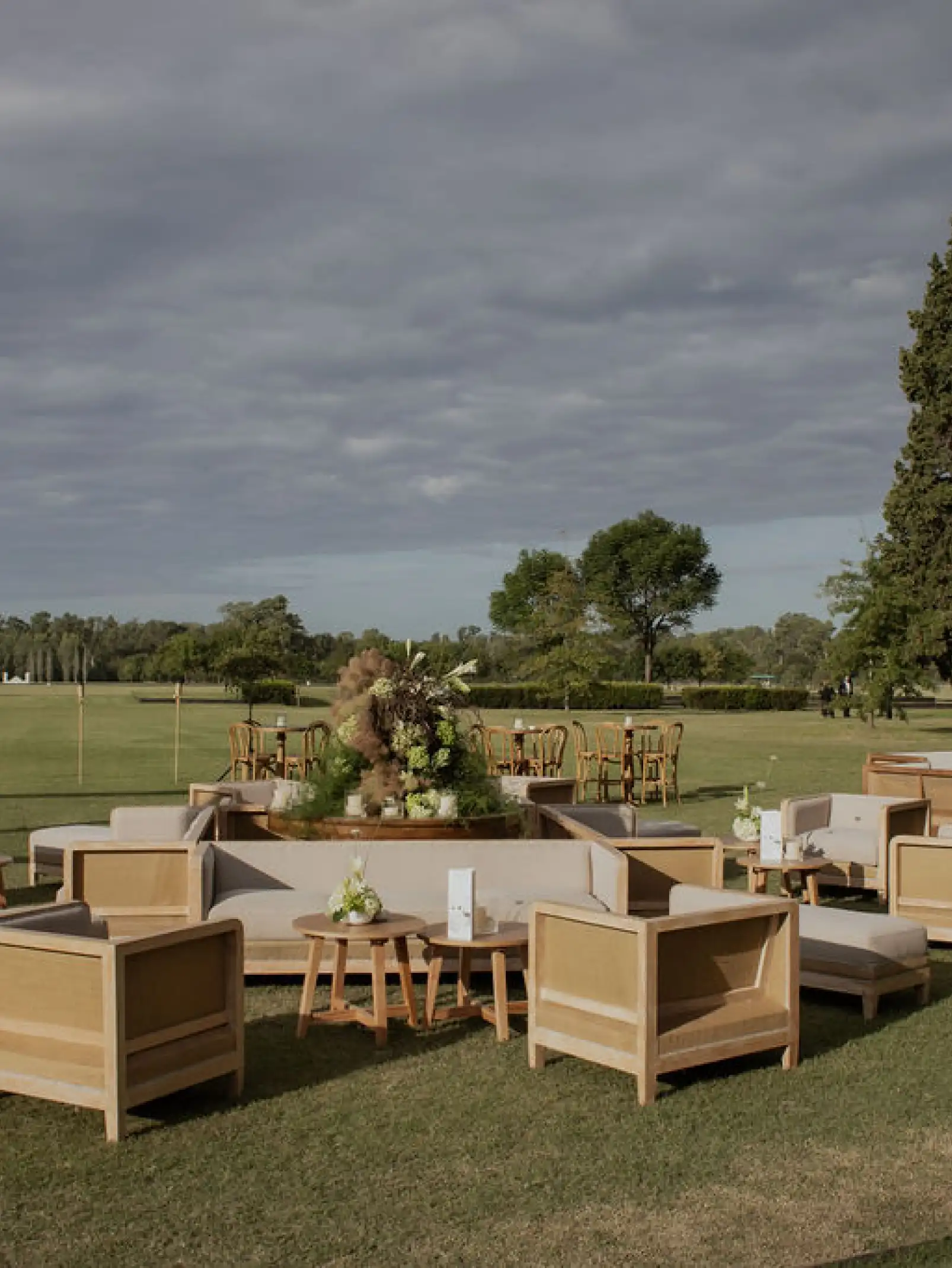 Zona de livings de madera con arreglos florales verdes para eventos de exterior que combinan confort, diseño y conexión natural.