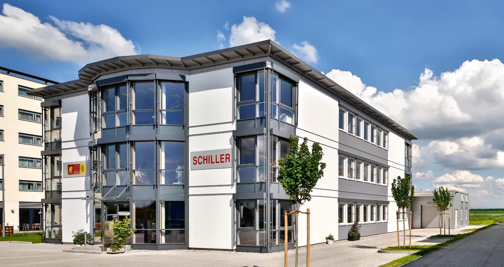 Moderne Bürogebäude an einem sonnigen Tag mit blauem Himmel und Wolken. Schiller-Logo ist gut sichtbar.