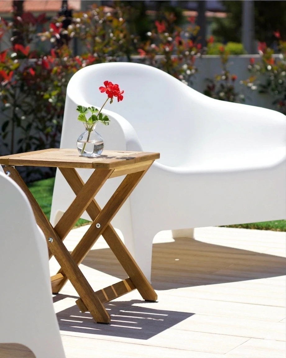 A small chair and table with a flower next to a swimming pool