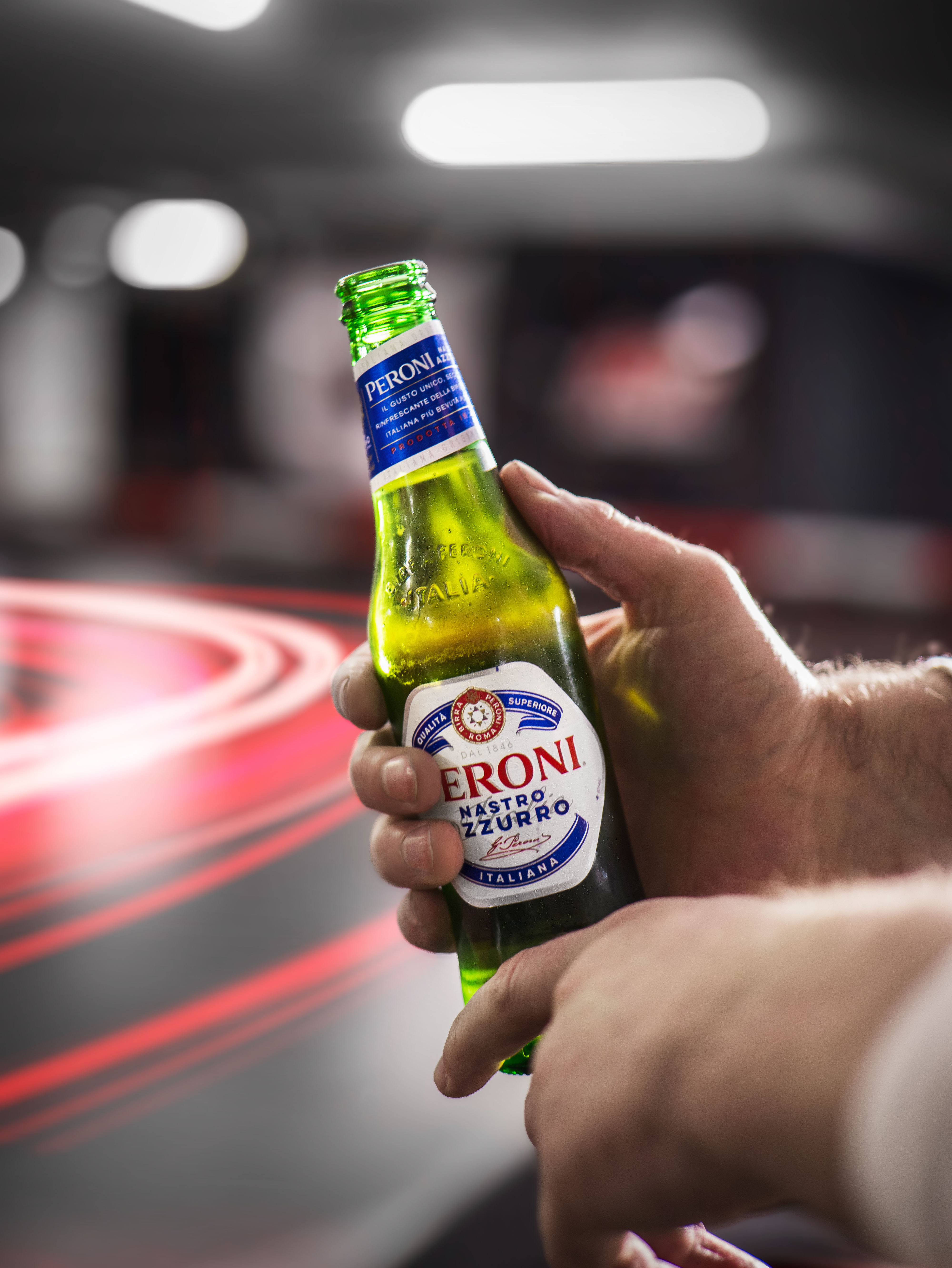 A close-up of a hand holding a green bottle of beer against a blurred background with lights.