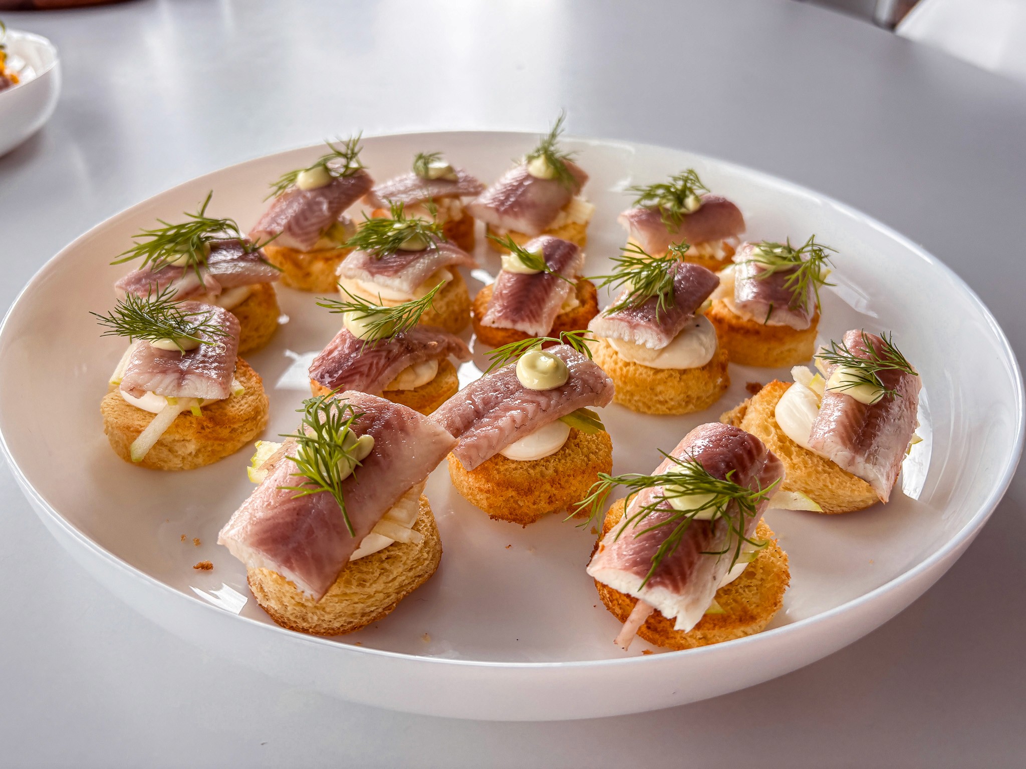 Plate with a seared salmon fillet topped with green herb garnish and sauce, served on a white dish placed on a dark green marble table beside a white candlestick.