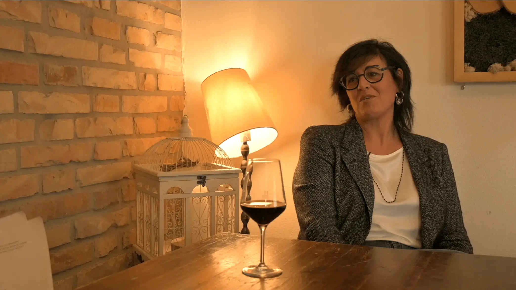 Donna seduta ad un tavolo con un calice di vino mentre viene intervistata per il documentario Donne in Bilico alla Locanda alla Mano di Forlimpopoli