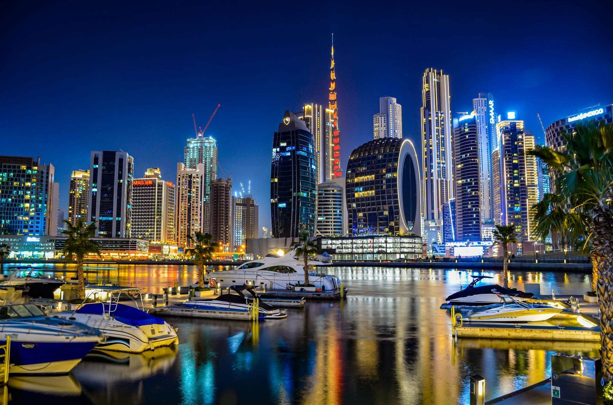 The night view of Dubai Marina with illuminated skyscrapers reflecting on the water and yachts docked along the marina.