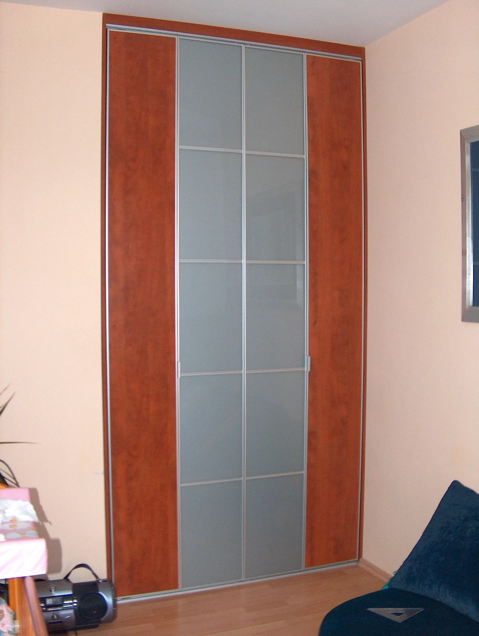 Stylowa szafa przesuwna łącząca fronty w kolorze ciepłego drewna z panelami z mlecznego szkła (lacomat).