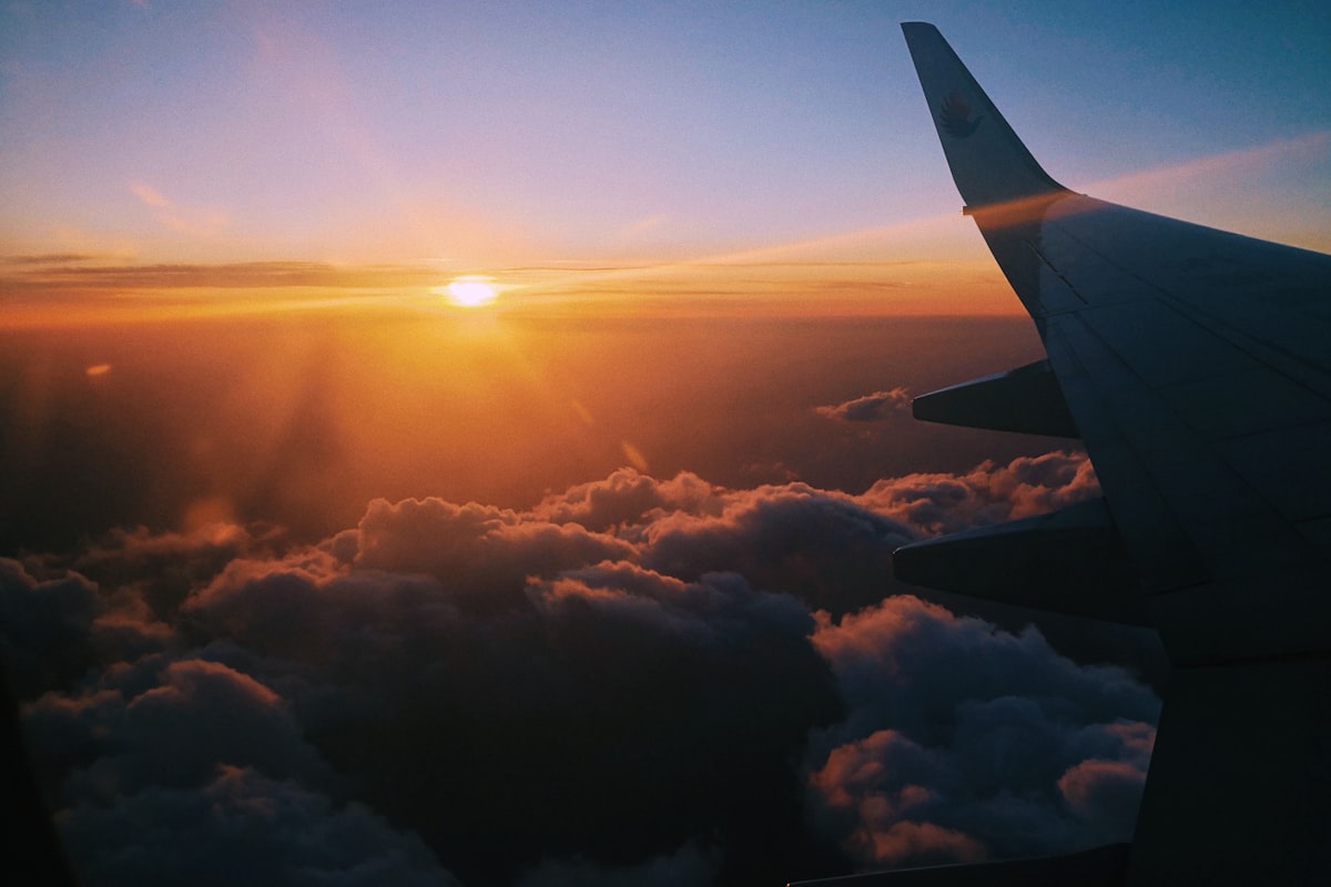 An airplane wing above golden clouds at sunset, en route to an international destination
