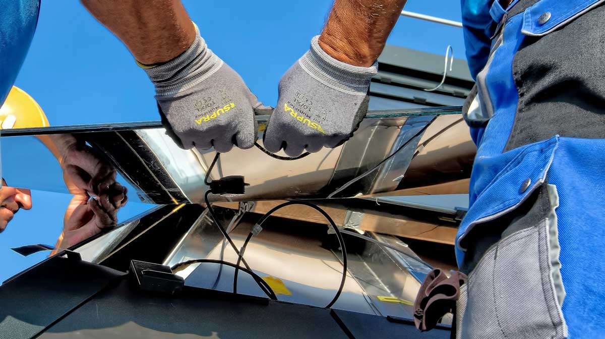 Monteur mit Sicherheitsausrüstung arbeitet an Solarmodulen auf dem Dach