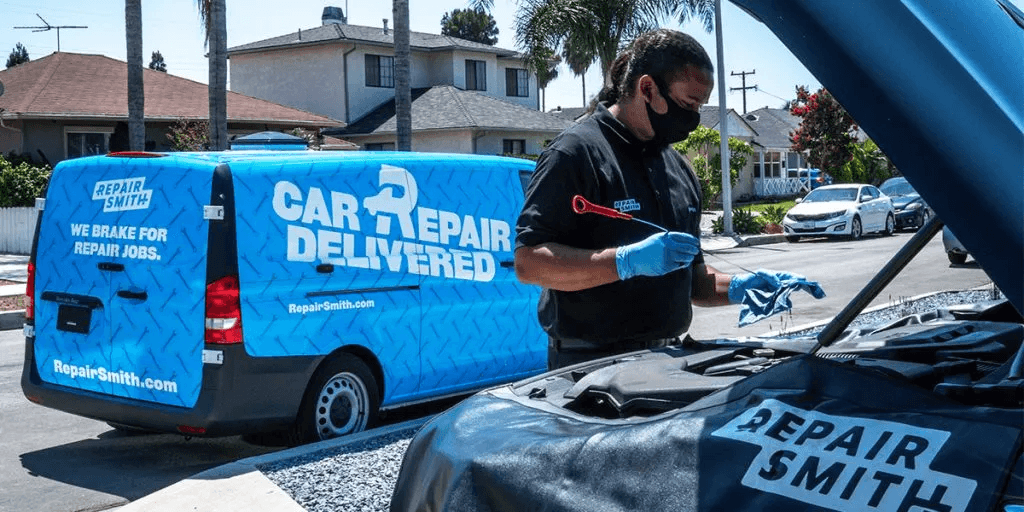 Mobile mechanic checking oil level gauge with RepairSmith truck in the background.