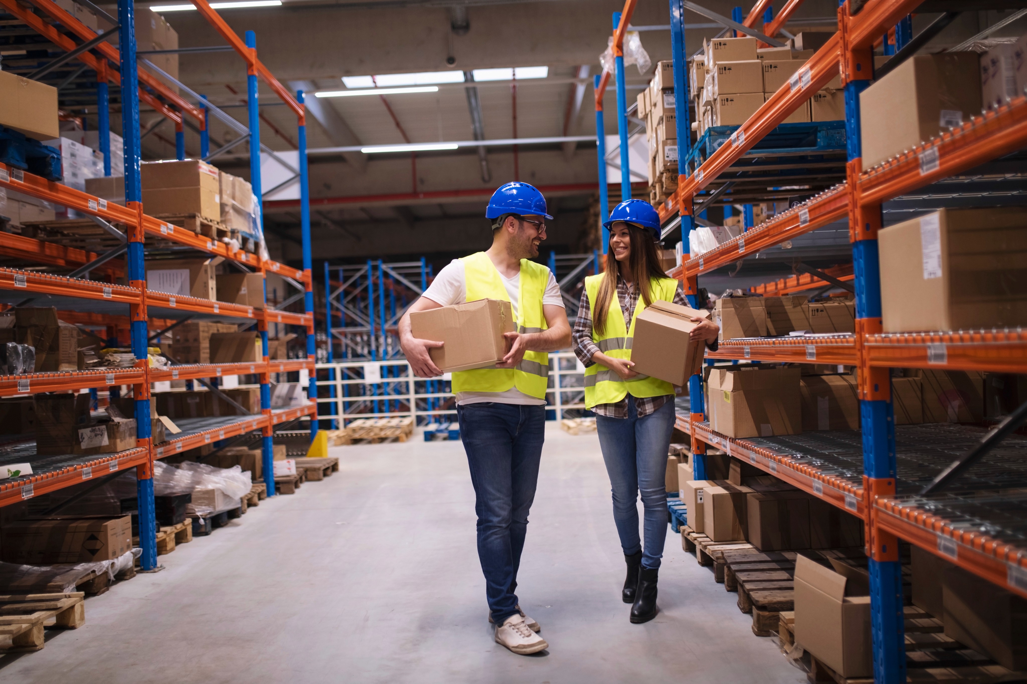 Man and woman logistics team carrying boxes in a modern warehouse.