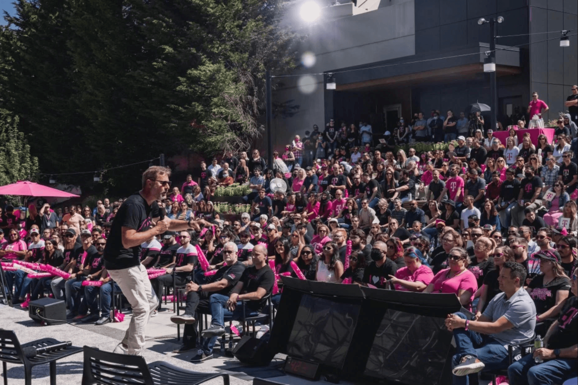 A speaker engages a diverse, magenta clad audience at the outdoor amphitheater during an all-staff gathering.